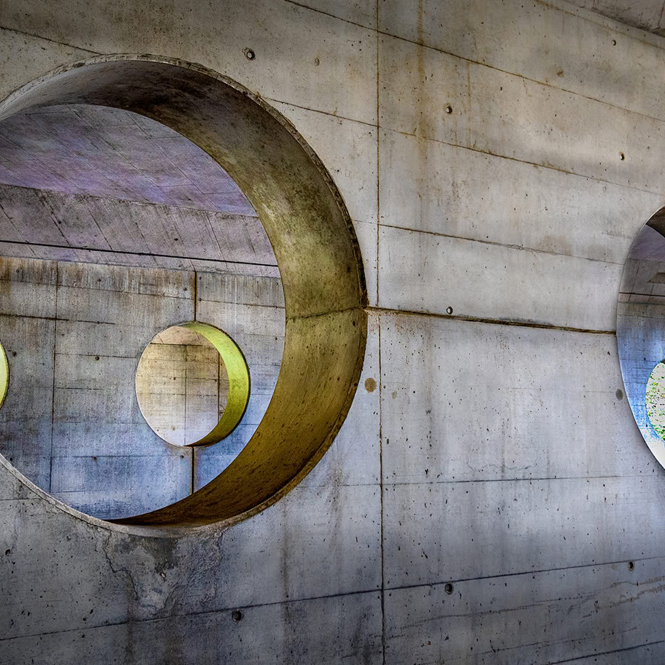 Deux ouvertures circulaires dans un mur en béton, laissant passer la lumière.