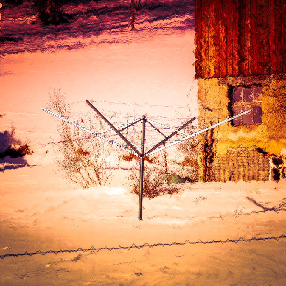 Un étendoir à linge en métal dans un paysage enneigé, avec une maison en arrière-plan.