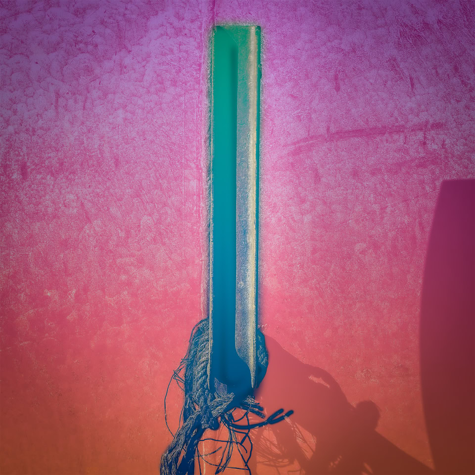 Un poteau vert avec des fils à la base, sur un fond dégradé de rose et orange.