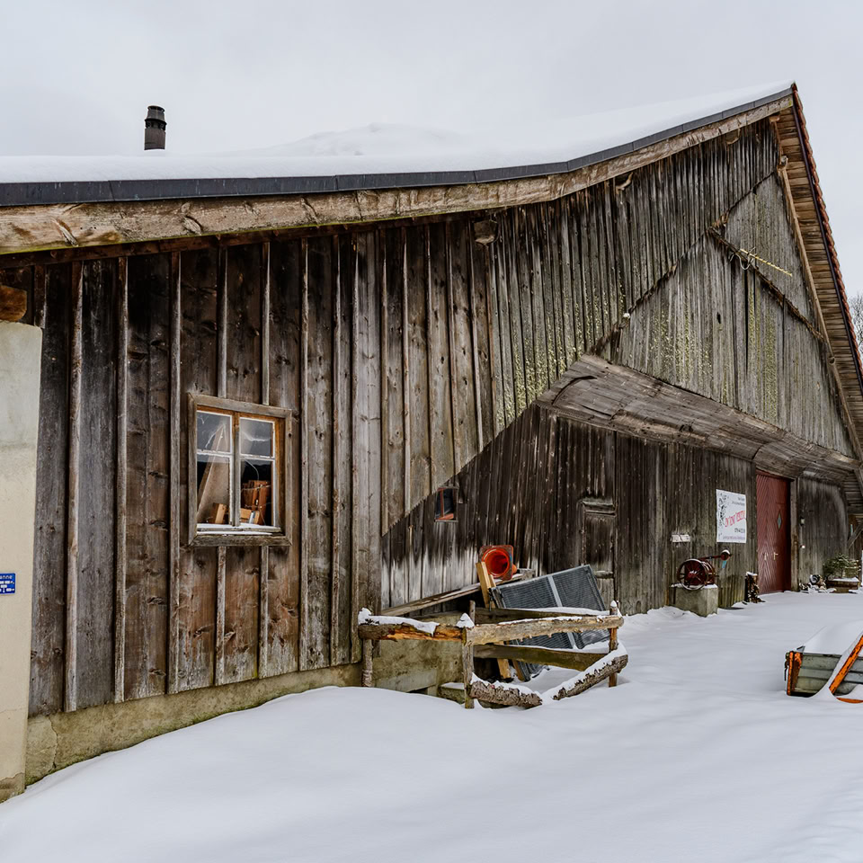 Bâtiment en bois avec un toit incliné, entouré de neige, avec des arbres en arrière-plan.