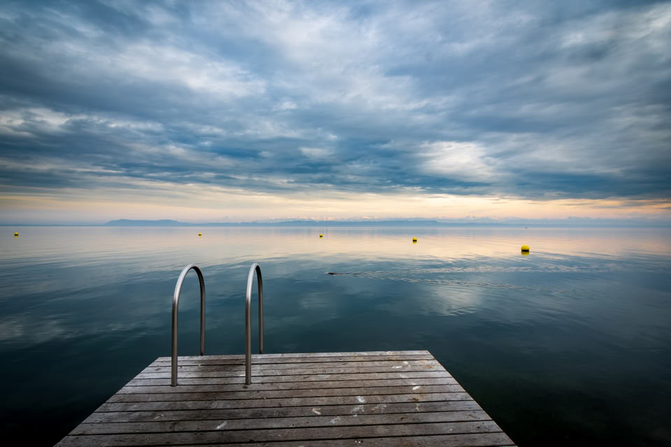 Plateforme en bois avec une échelle menant à un lac calme sous un ciel nuageux.