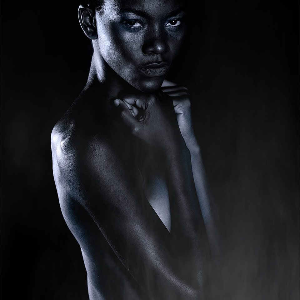 Personne posant dans l'obscurité avec un éclairage dramatique, regardant vers l'avant, le corps partiellement couvert d'ombres.