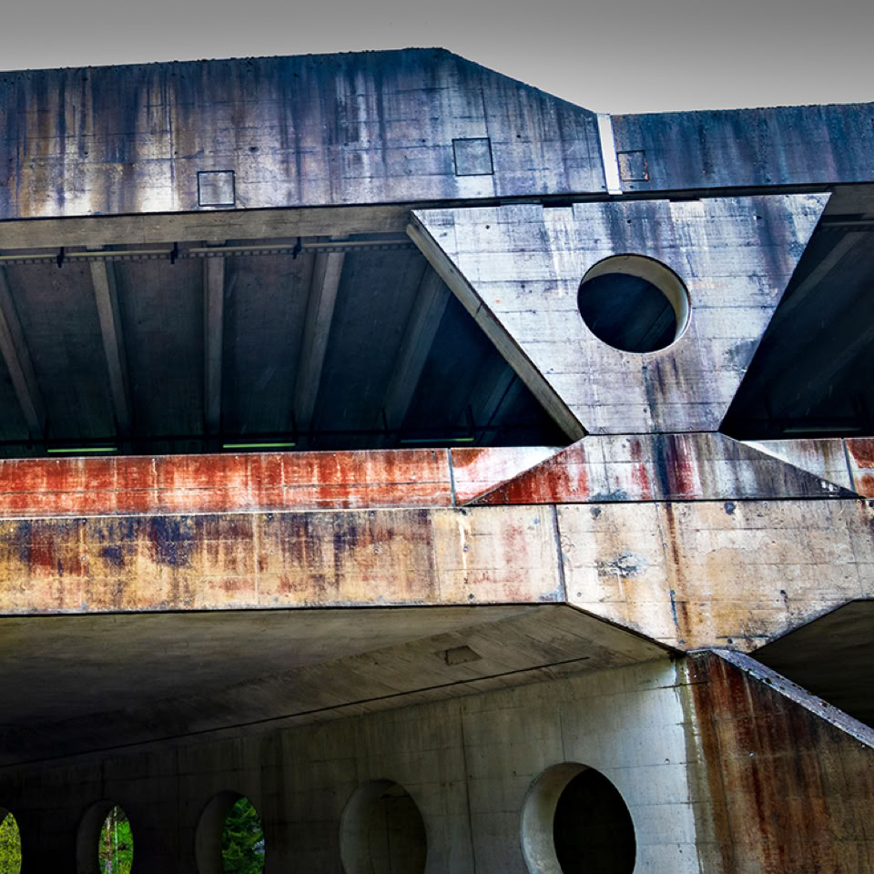 A close-up view of a weathered concrete bridge with visible rust stains and structural beams.