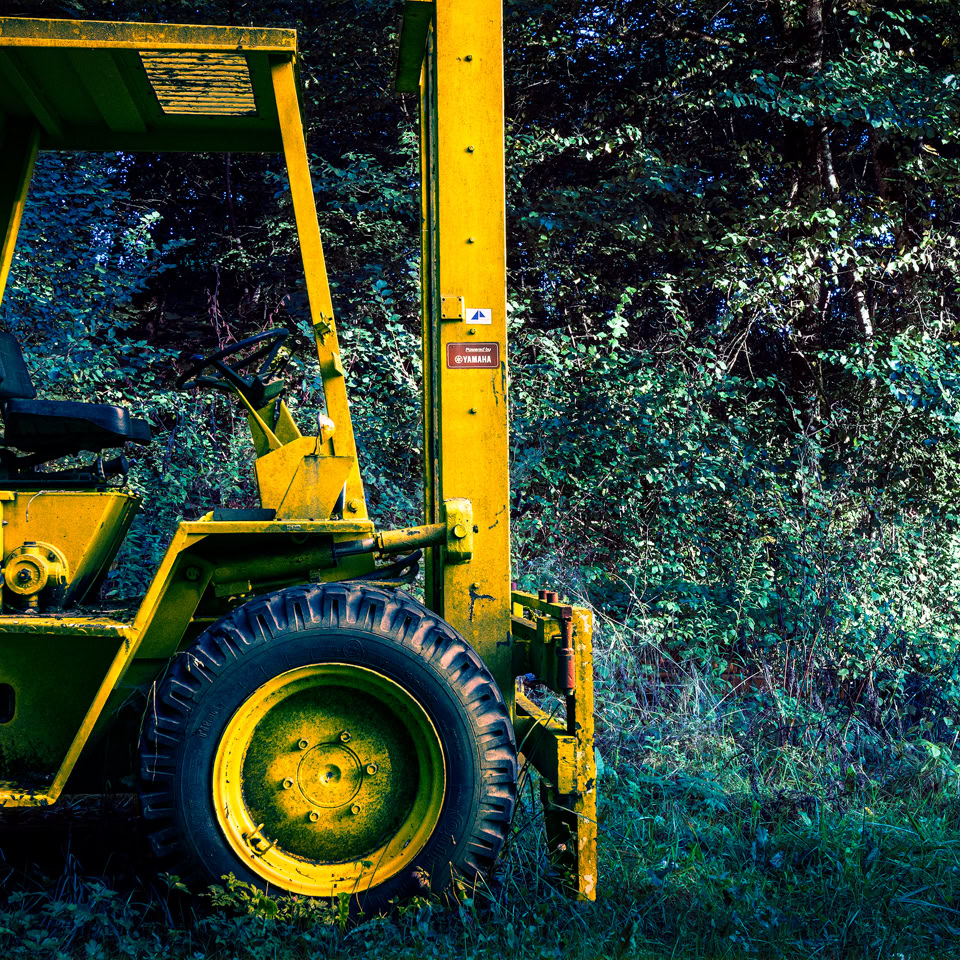 Chariot élévateur jaune stationné sur de l'herbe, avec des arbres en arrière-plan.