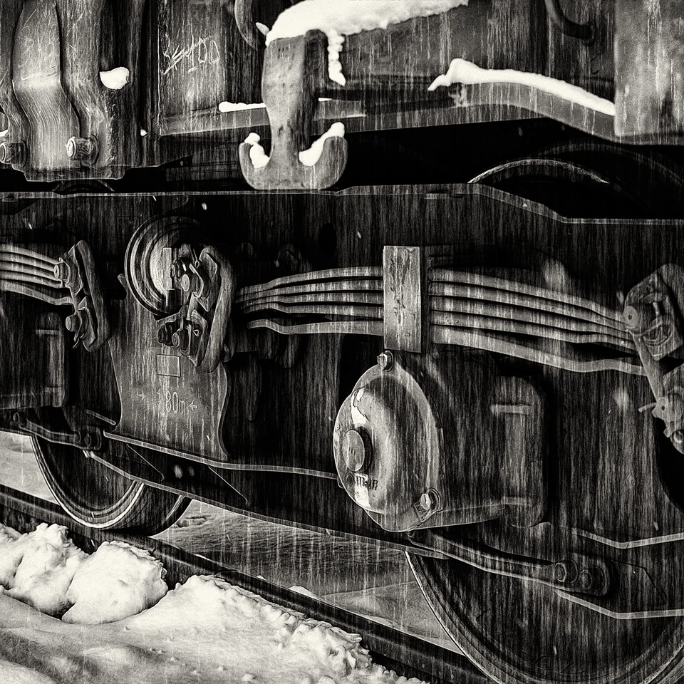 Vue rapprochée des roues et du châssis d'un wagon de train sur des rails enneigés.