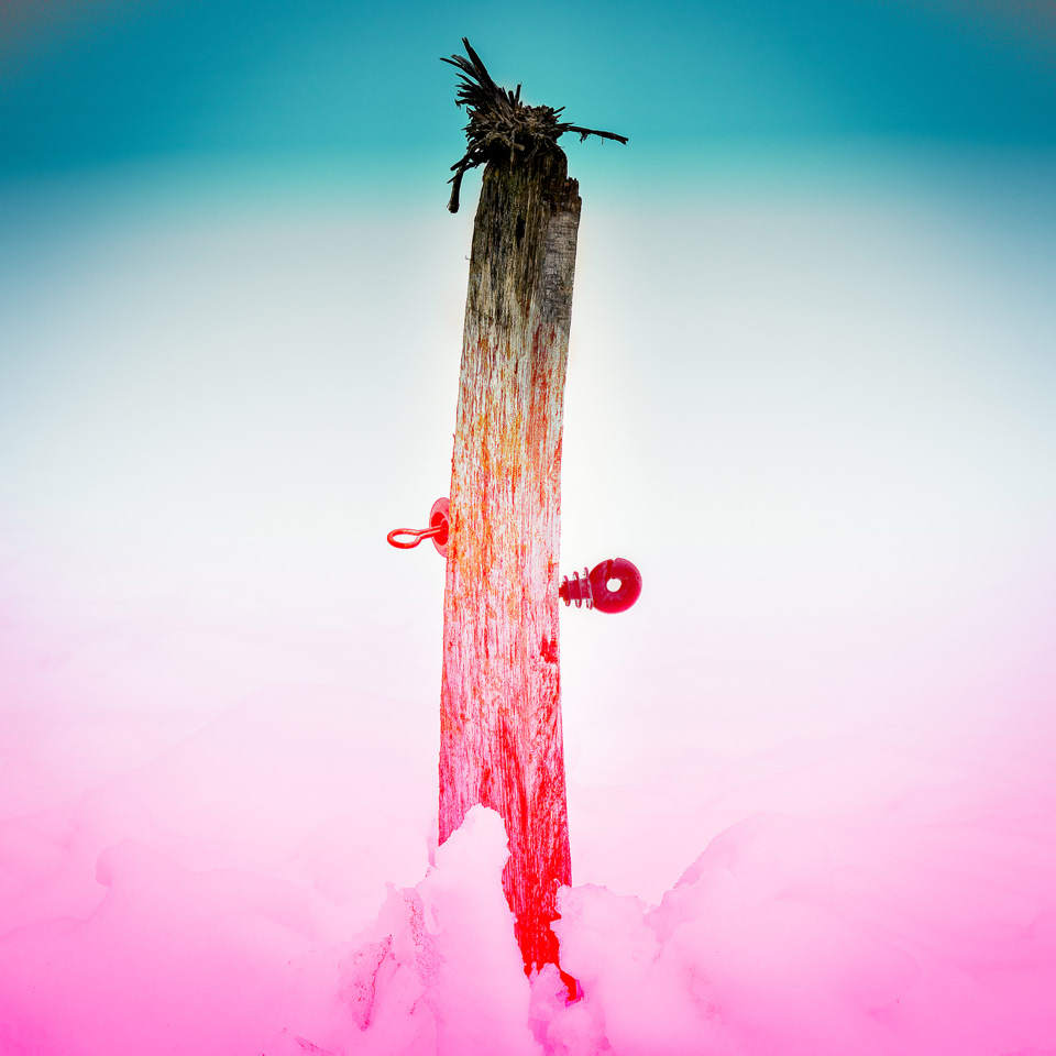 Un poteau en bois planté dans la neige avec un ciel dégradé de bleu et rose en arrière-plan.