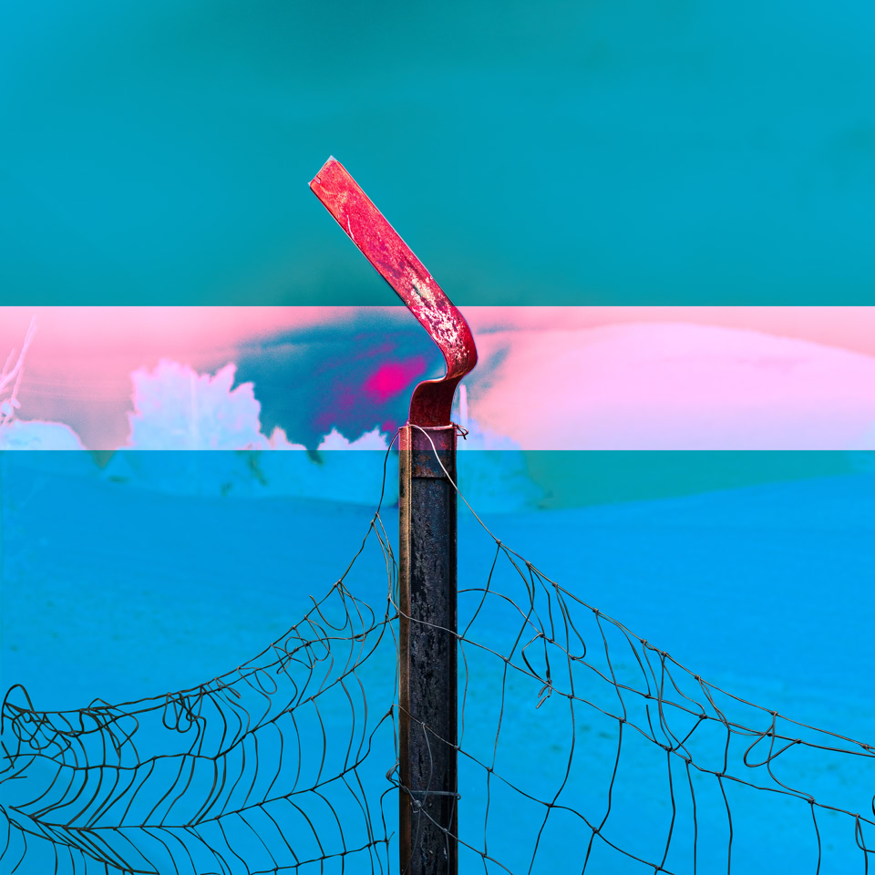 Un poteau métallique avec un sommet incliné et rouillé, entouré de fil de fer barbelé, sur un fond de ciel bleu et rose.